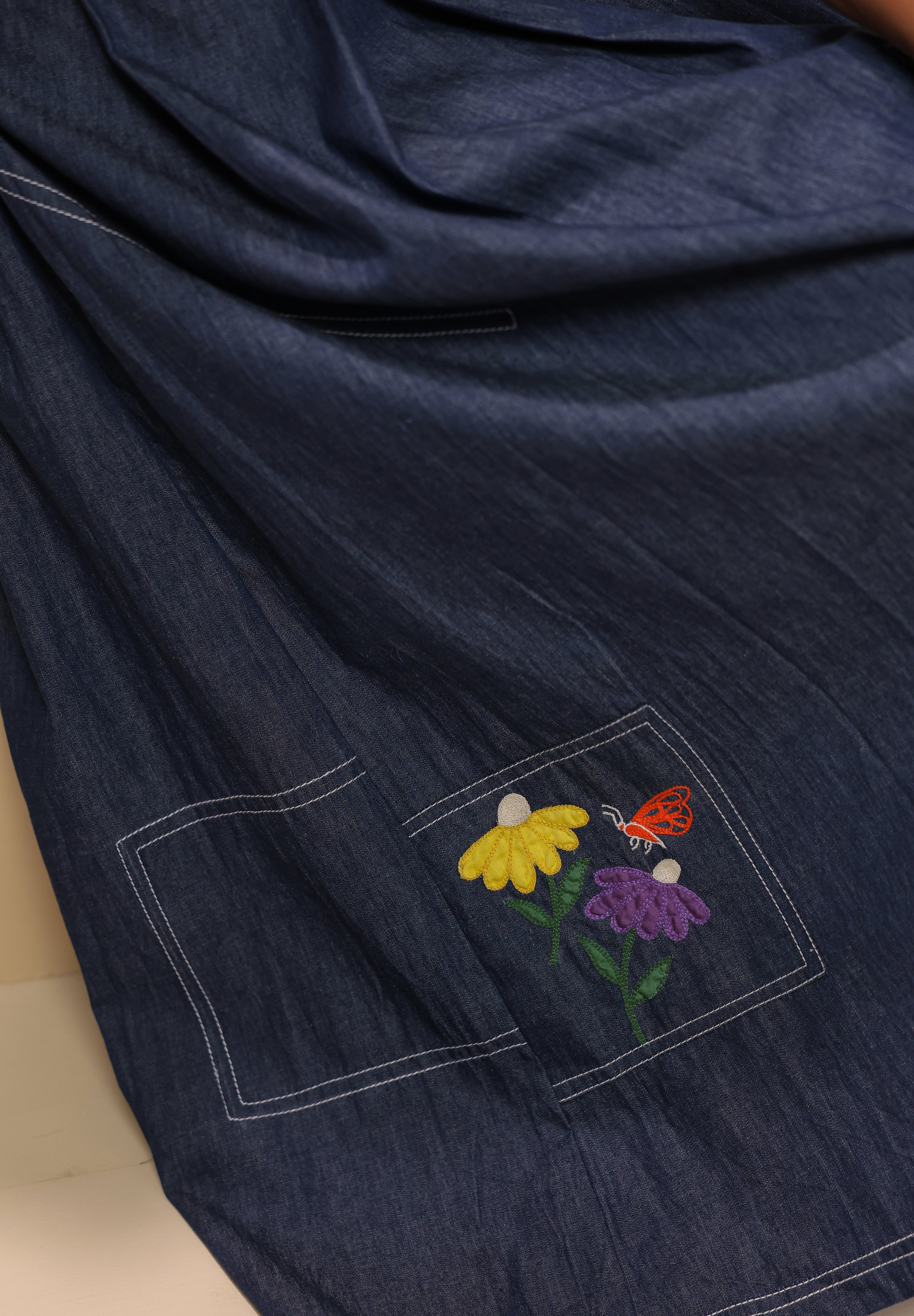 Close-up of pocket patch embroidery featuring yellow and purple florals with an orange butterfly — inspired by meadows in bloom.