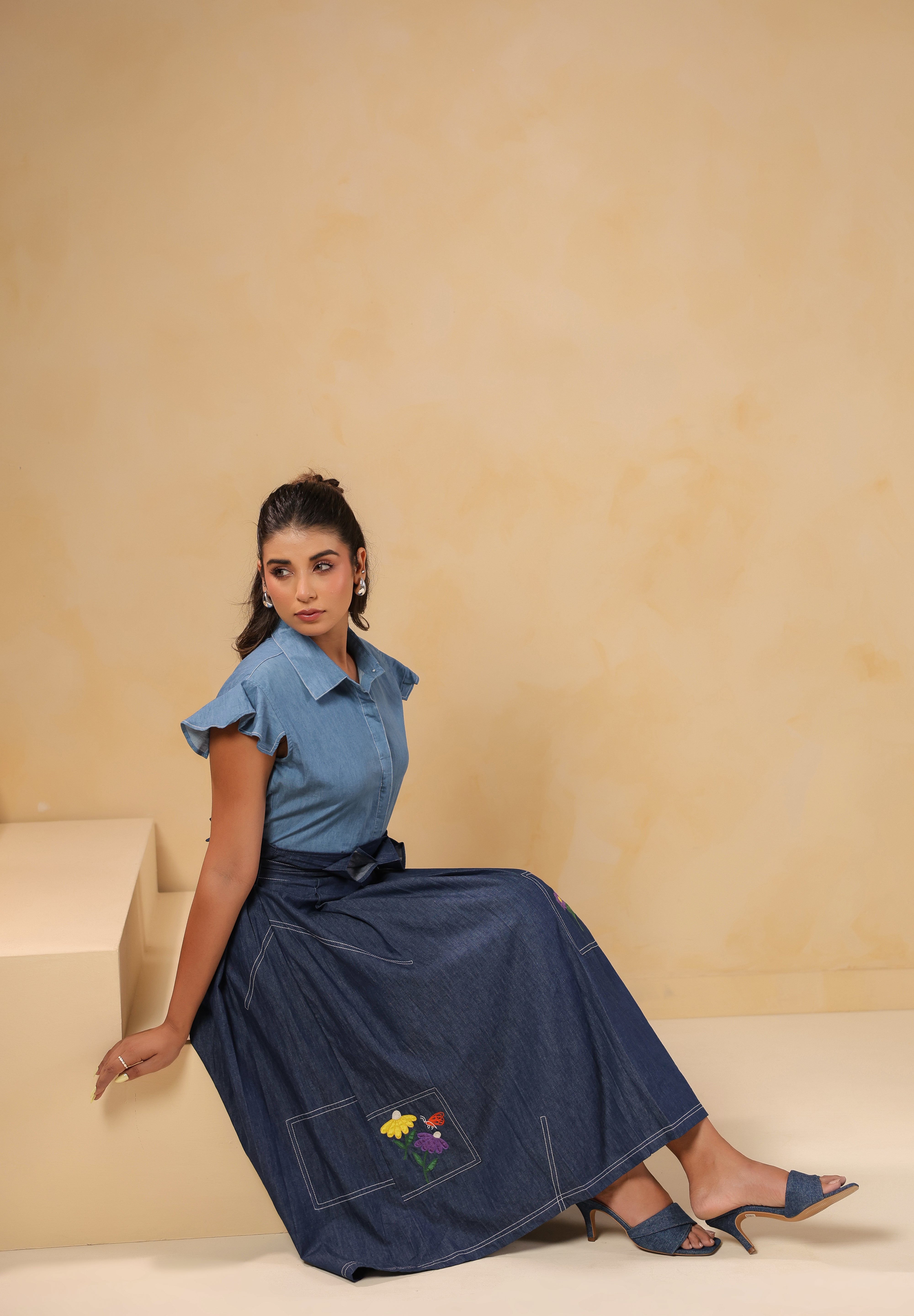 Side-seated pose of model in Ridah’s Meadowflair Coord Set highlighting embroidered motifs, pleats, and ruffle sleeve fall.