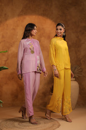 Two women in traditional outfits standing against a brown background