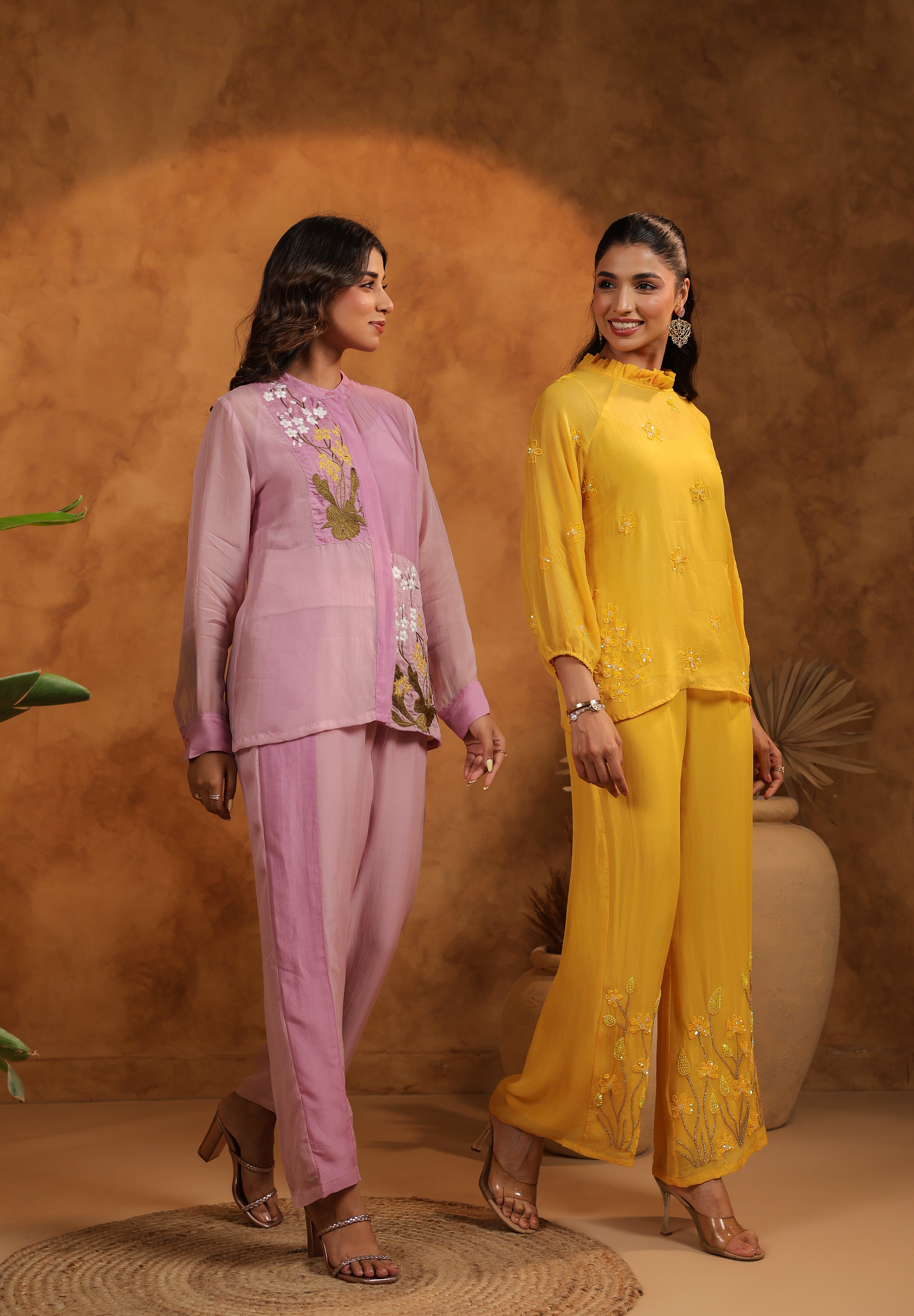 Two women in traditional outfits standing against a brown background