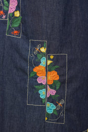 Embroidery detail of colorful floral motifs on denim dress.