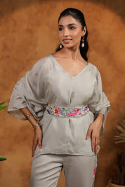 Woman wearing a light gray outfit with a floral belt against a brown background
