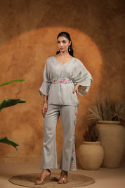 Woman in a light gray outfit with floral details standing against a warm-toned background