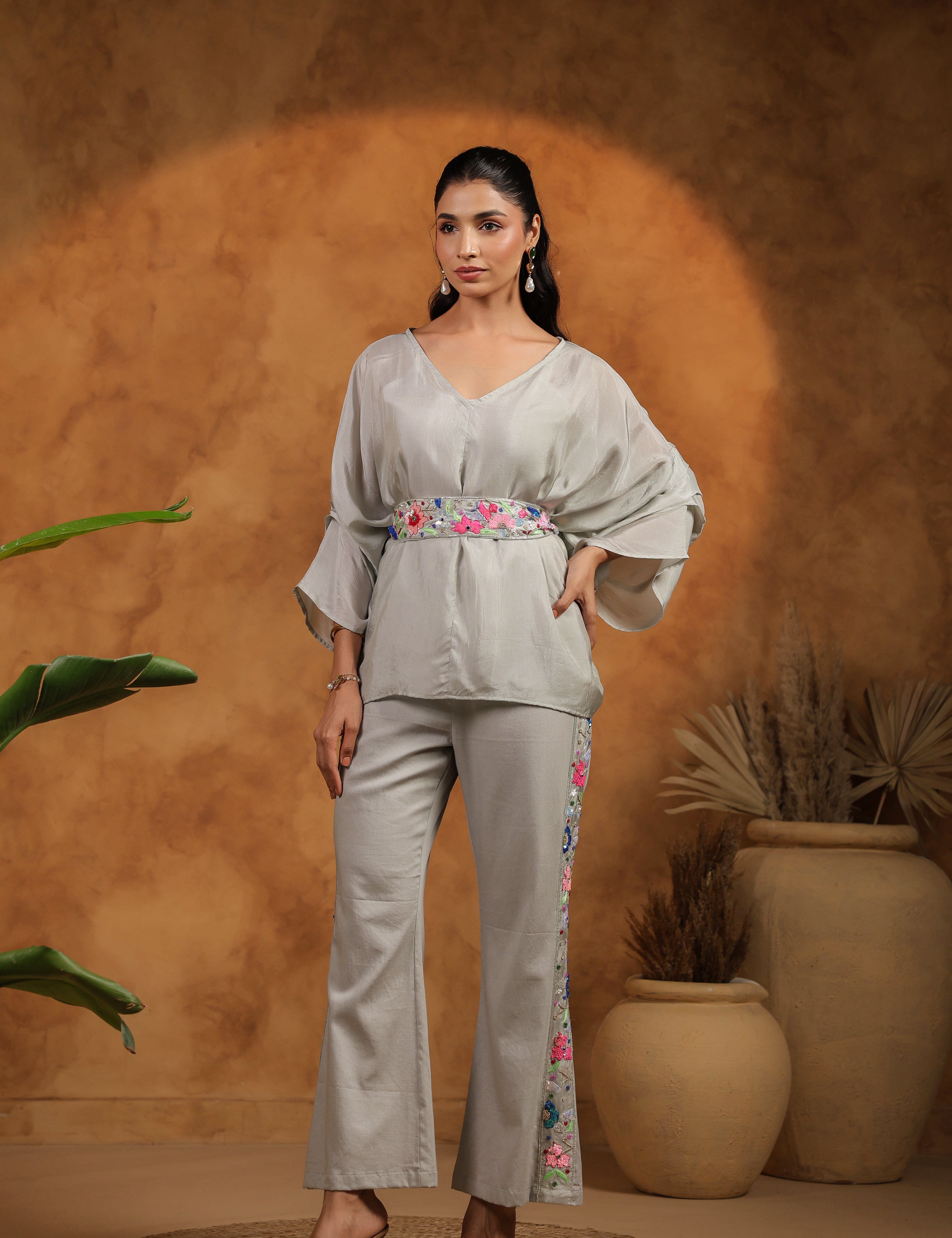 Woman in a light gray outfit with floral details standing against a warm-toned background