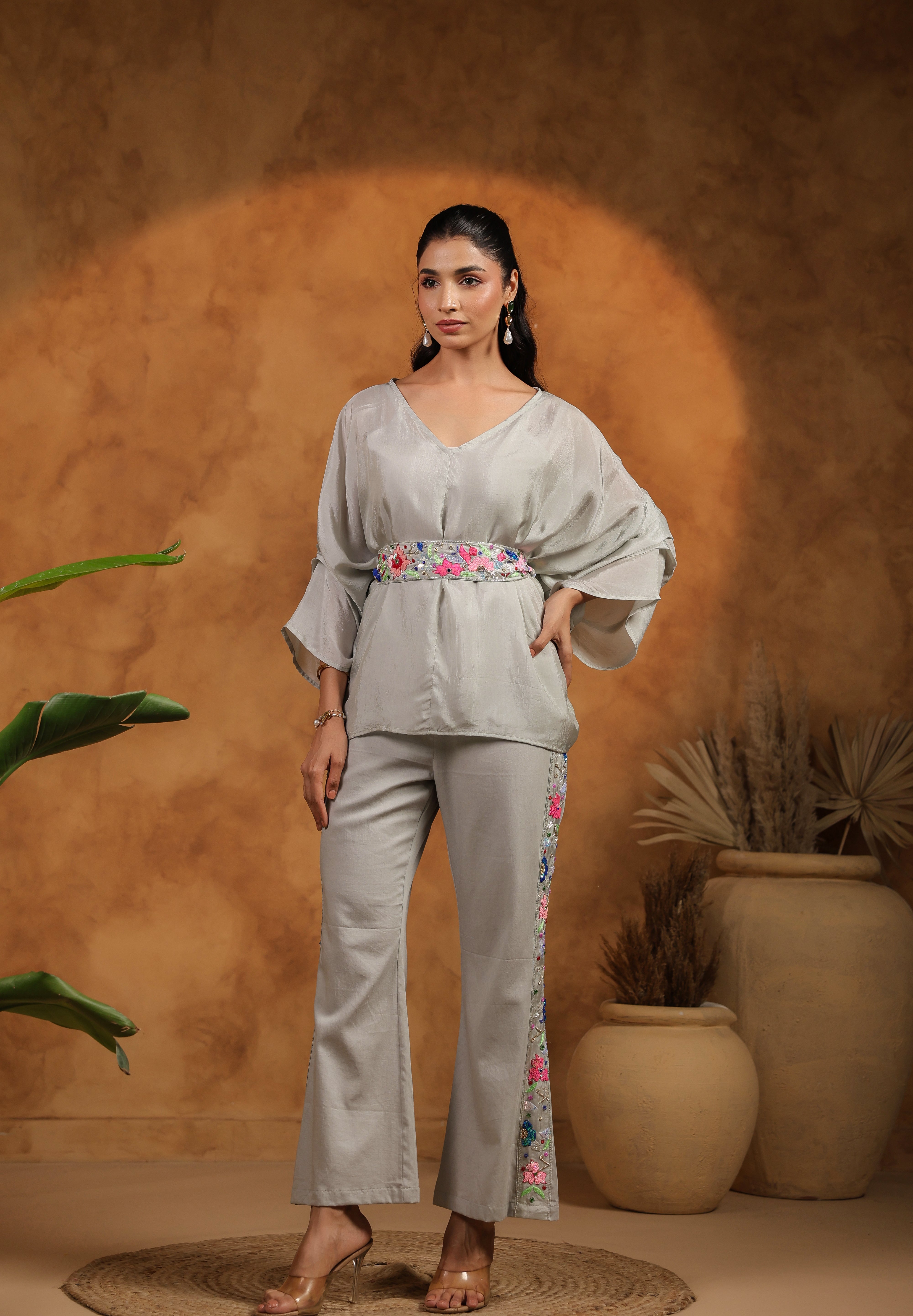 Woman in a light gray outfit with floral details standing against a warm-toned background