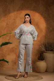 Woman wearing a light gray outfit with floral embroidery against a warm brown background