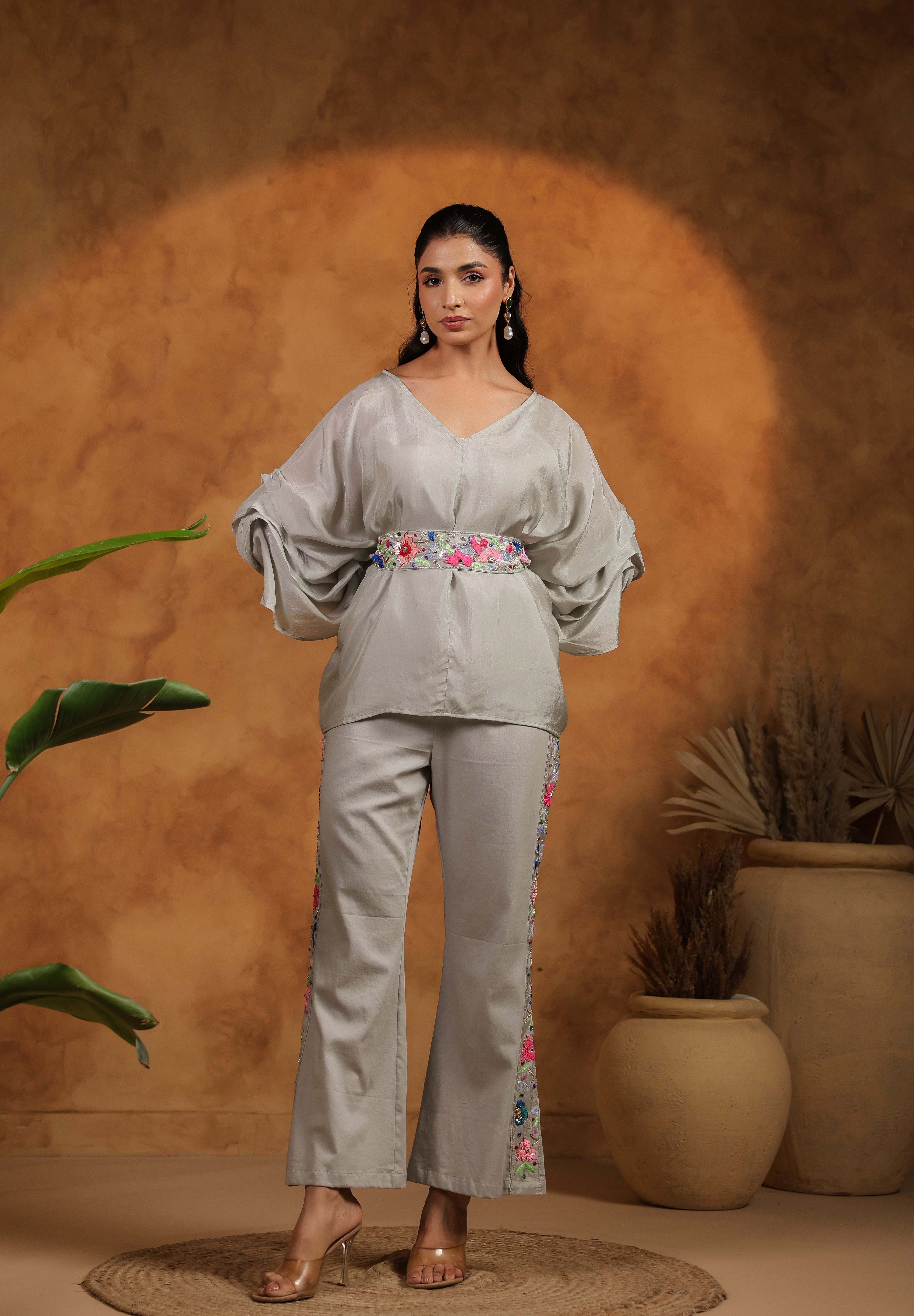 Woman wearing a light gray outfit with floral embroidery against a warm brown background