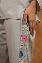 Close-up of a person wearing a light-colored outfit with colorful floral embroidery on a plain background