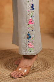 Close-up of gray pants with floral embroidery on a textured brown surface