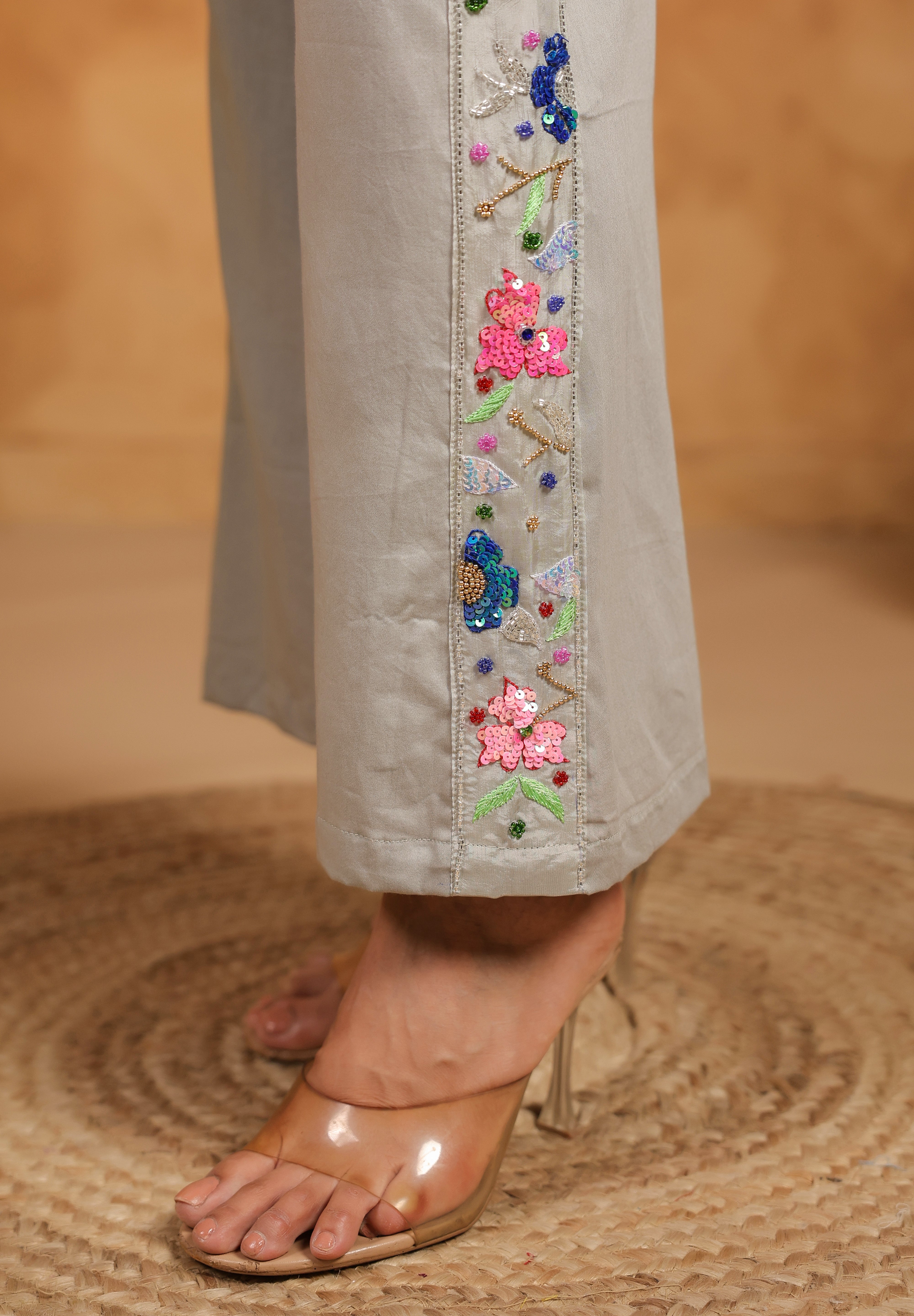 Close-up of gray pants with floral embroidery on a textured brown surface