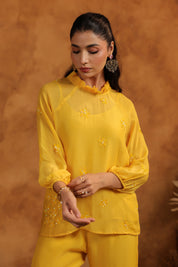 Woman wearing a yellow outfit with intricate designs against a brown background