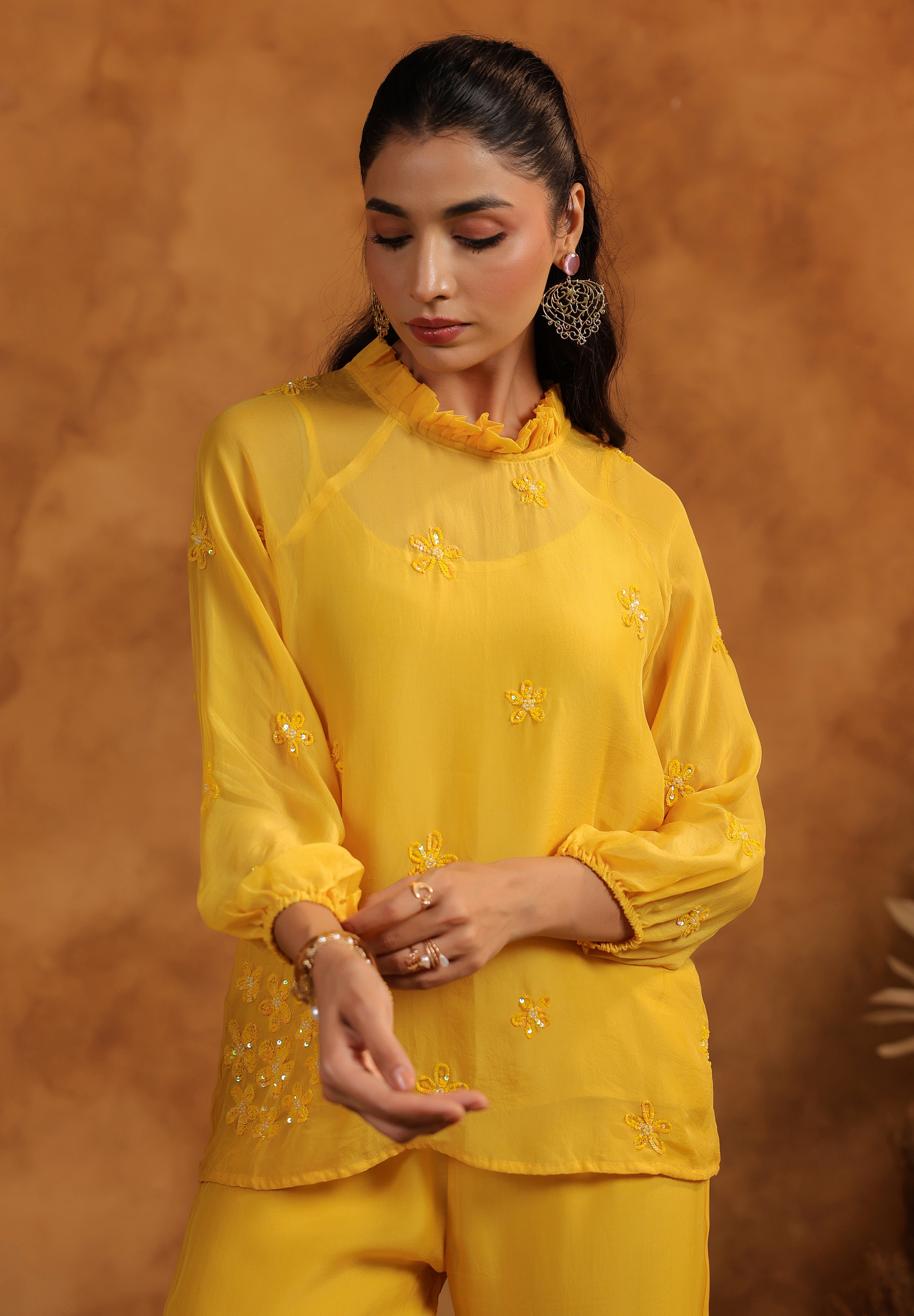 Woman wearing a yellow outfit with intricate designs against a brown background