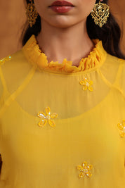 Yellow top with floral embellishments worn by a model against a neutral background