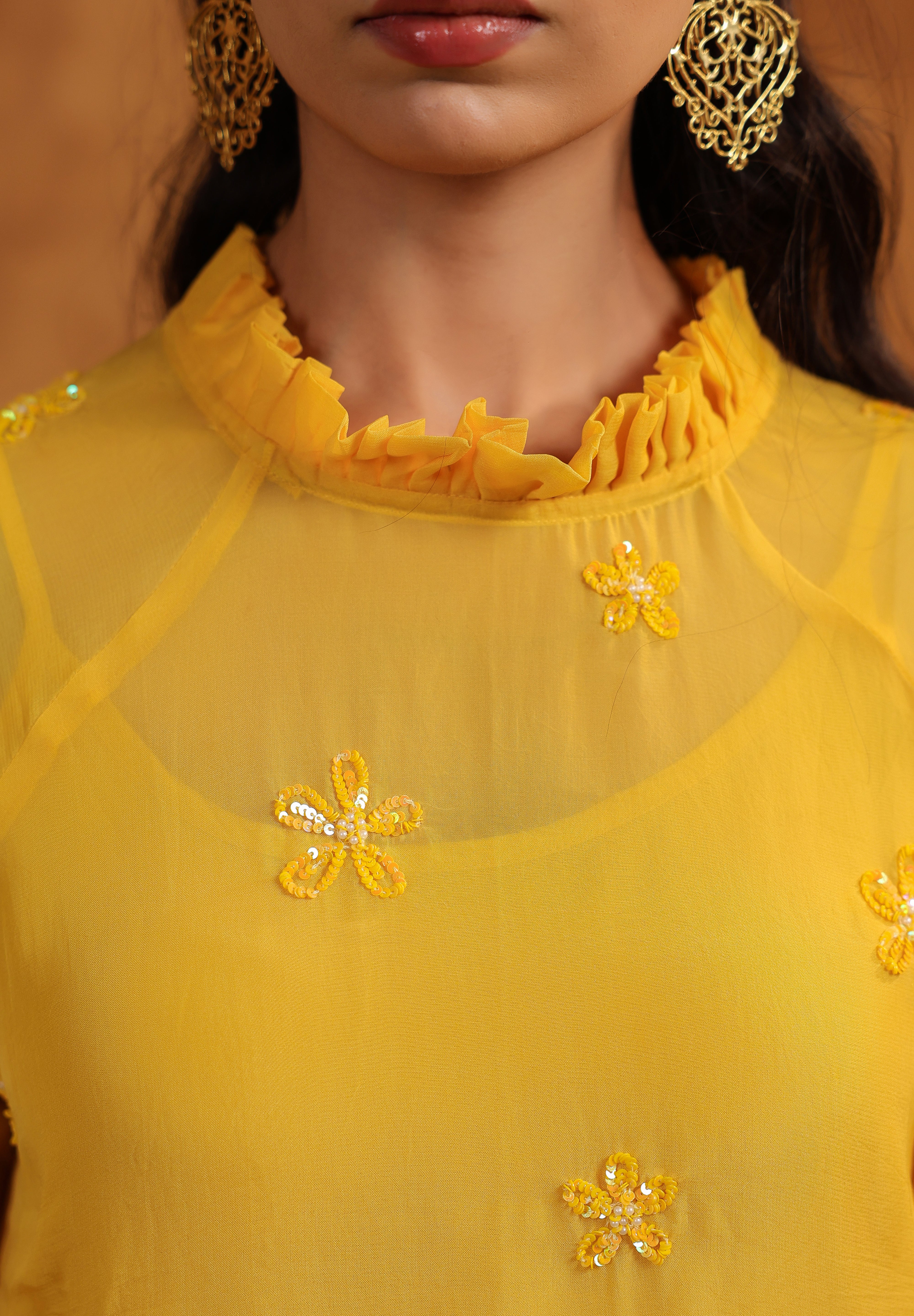 Yellow top with floral embellishments worn by a model against a neutral background