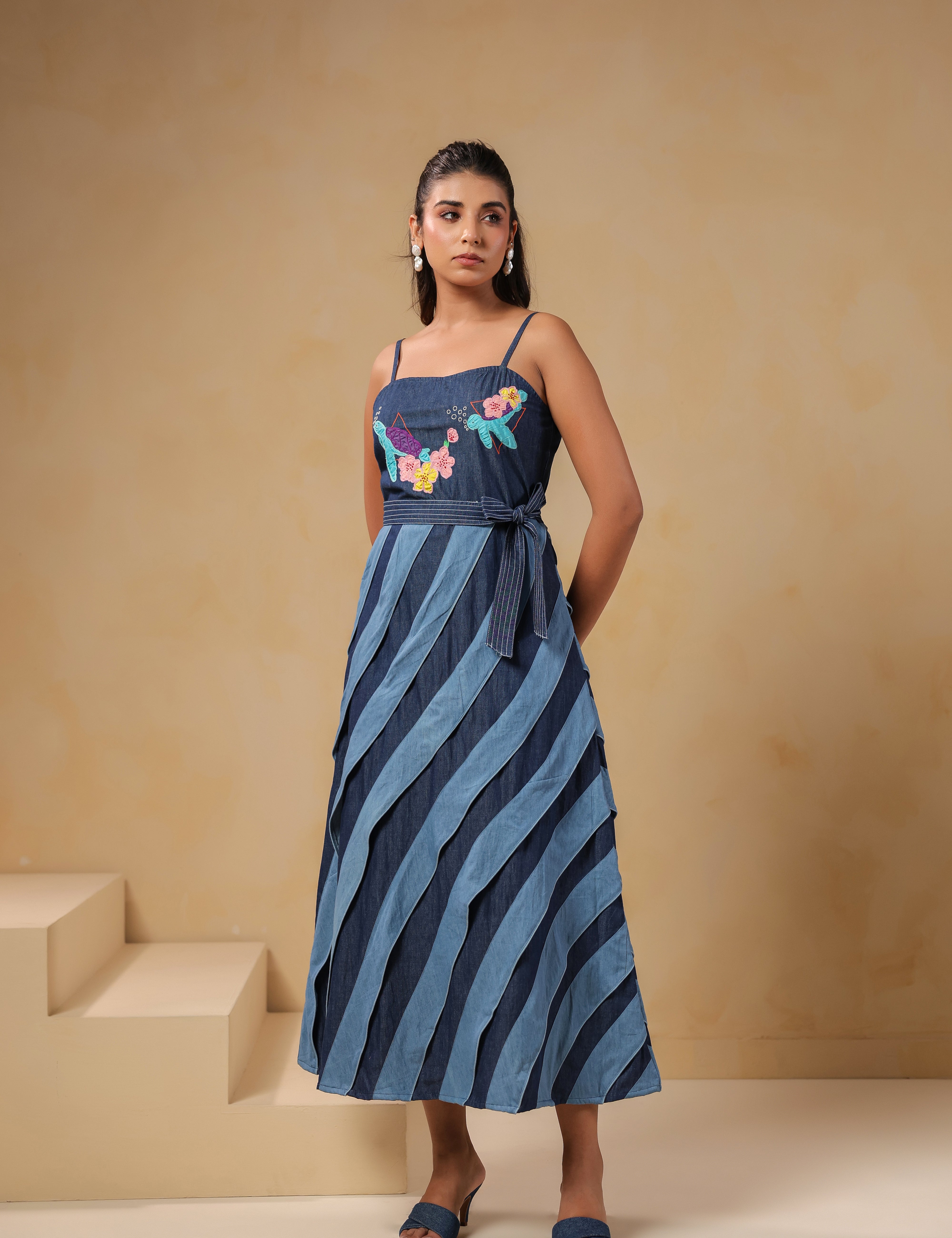 Front view of Turtletide Flare Dress, sleeveless denim midi dress with spiral panel detailing and colorful turtle-and-floral embroidery on bodice