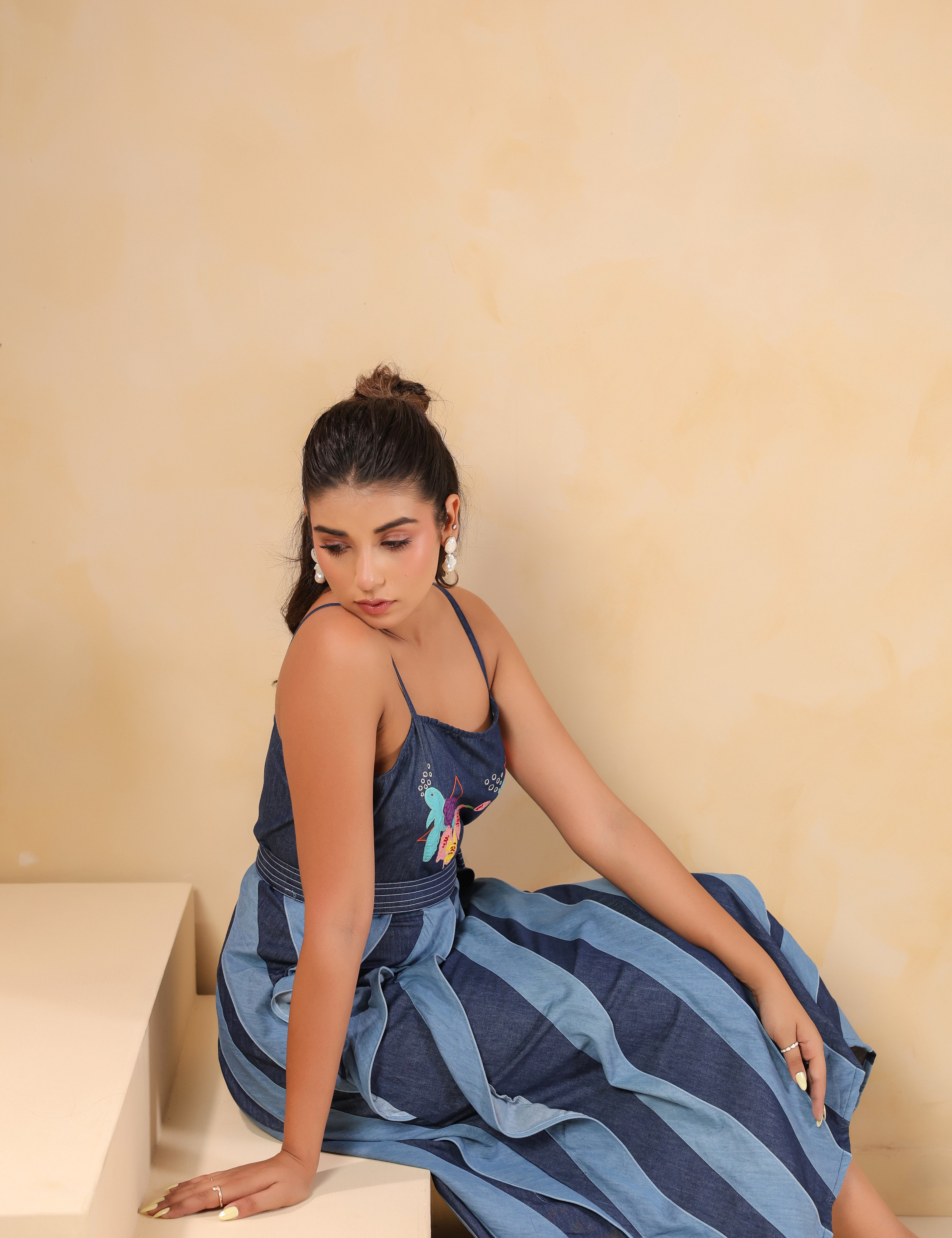 Model sitting in Turtletide Flare Dress highlighting layered denim spiral flare and multicolor embroidery