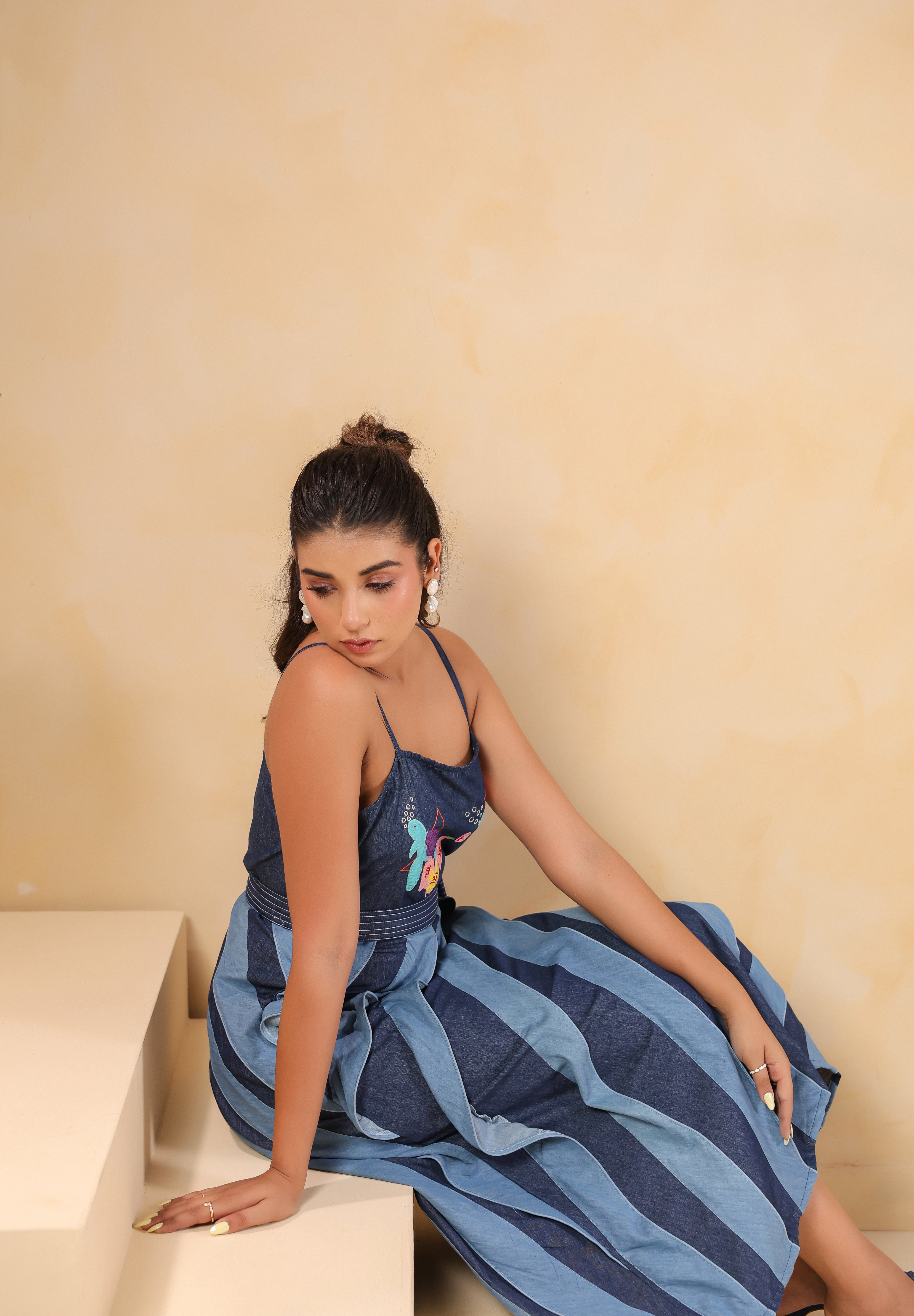 Model sitting in Turtletide Flare Dress highlighting layered denim spiral flare and multicolor embroidery
